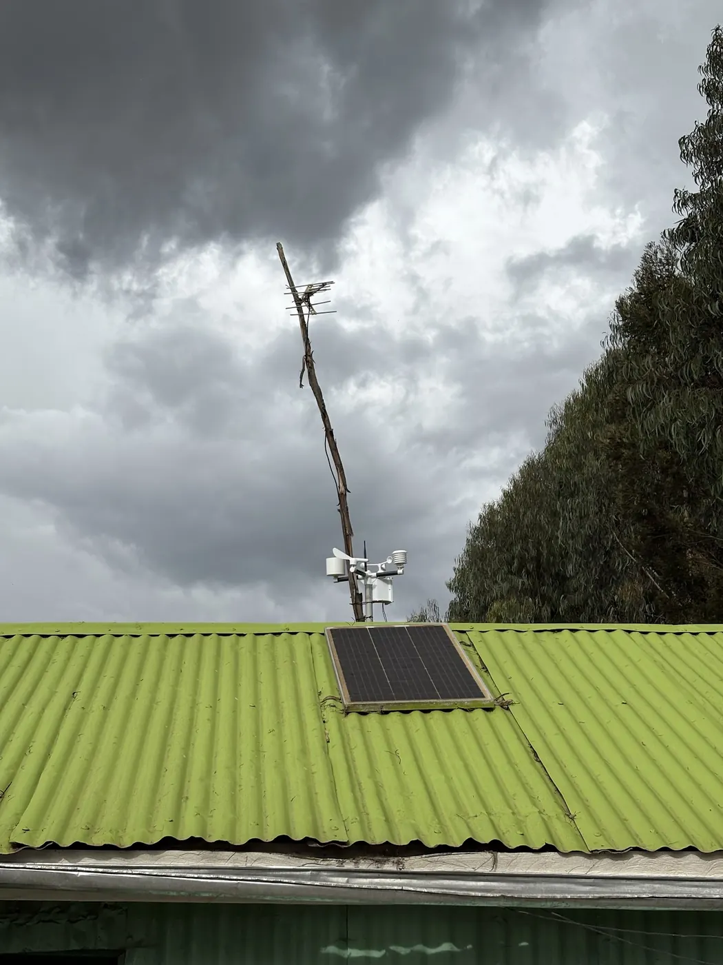 A weather station and solar panel on a green iron roof