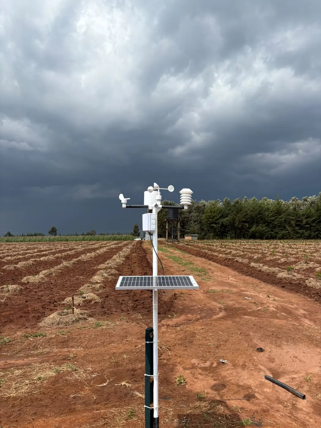 A solar-powered weather station on ridged red soil before rain